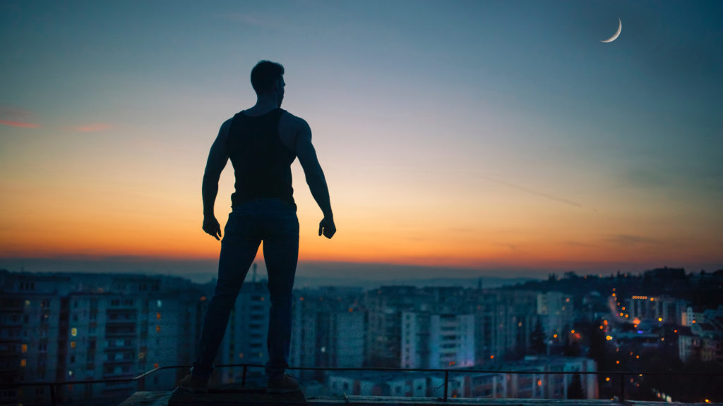 Photographic image of a muscular man standing at the top of a building look down upon the city below as though he were a superhero, used for a blog post about how internal links are the superhero of SEO.
